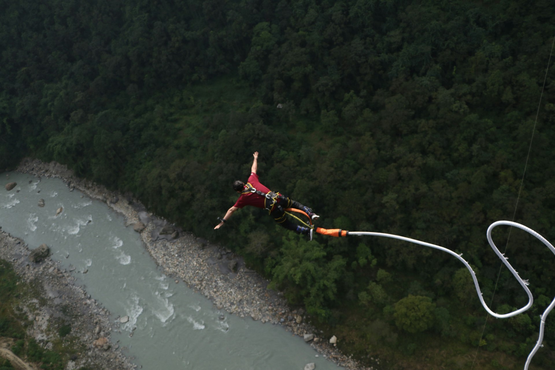 A man is parasailing over a river in the mountains